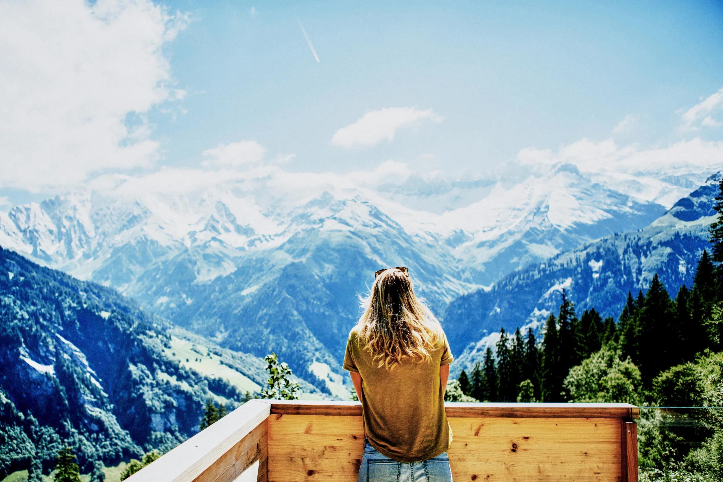 REAR VIEW OF WOMAN STANDING BY MOUNTAINS AGAINST SKY
