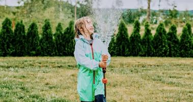 Young girl plays with garden hose